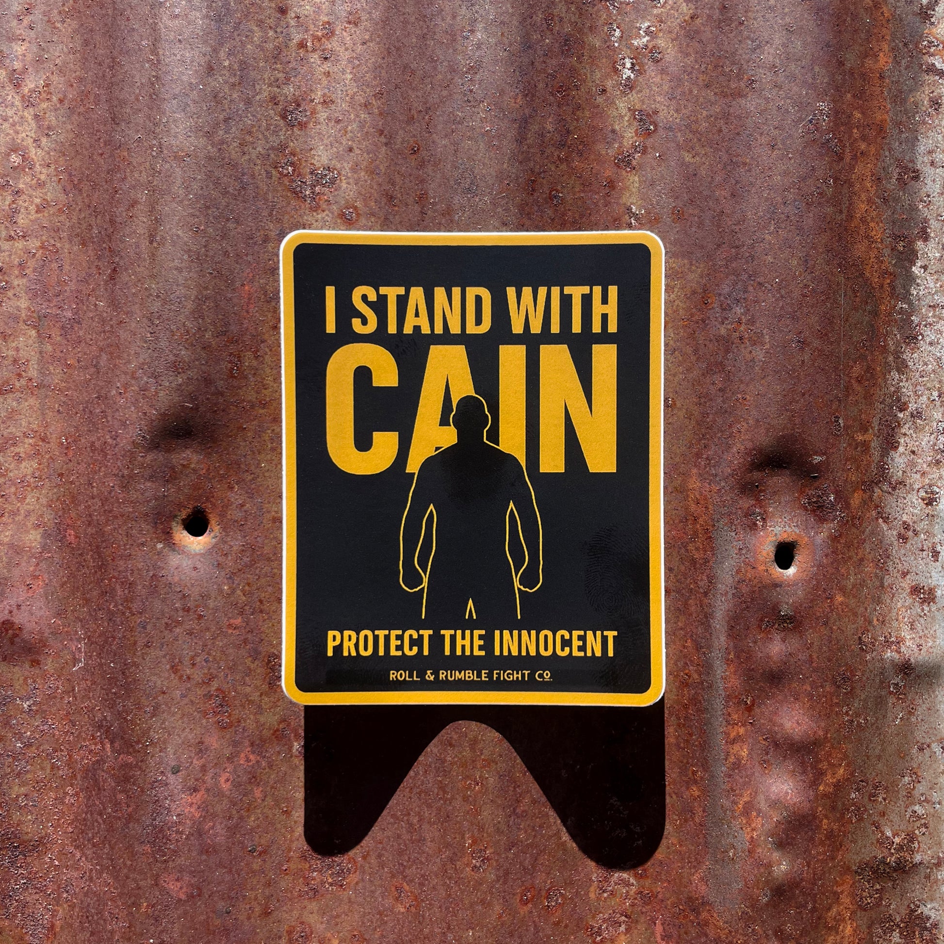 'I STAND WITH CAIN-PROTECT THE INNOCENT' sticker on a rusty metal background